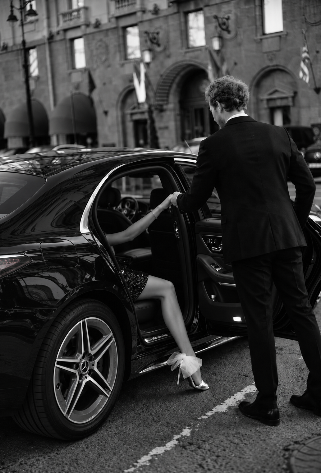 Schwarz-Weiß-Fotografie eines Chauffeurs, der einer Frau beim Aussteigen aus einem Mercedes-Benz hilft.