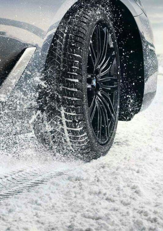 Nahaufnahme eines Autoreifens mit dunkler Felge und aufgewirbeltem Schnee.